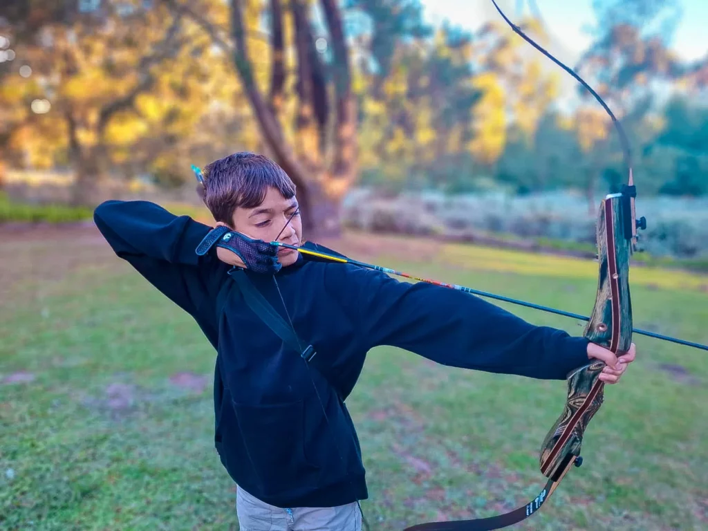 Boy practicing archery with recurve bow on grassy lawn